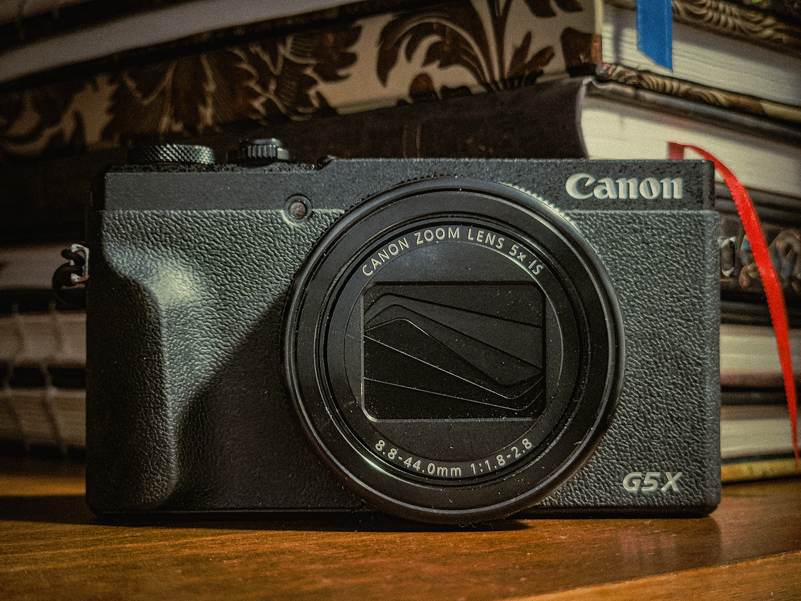 Canon PowerShot G5X II compact camera in front of a pile of sketchbooks.