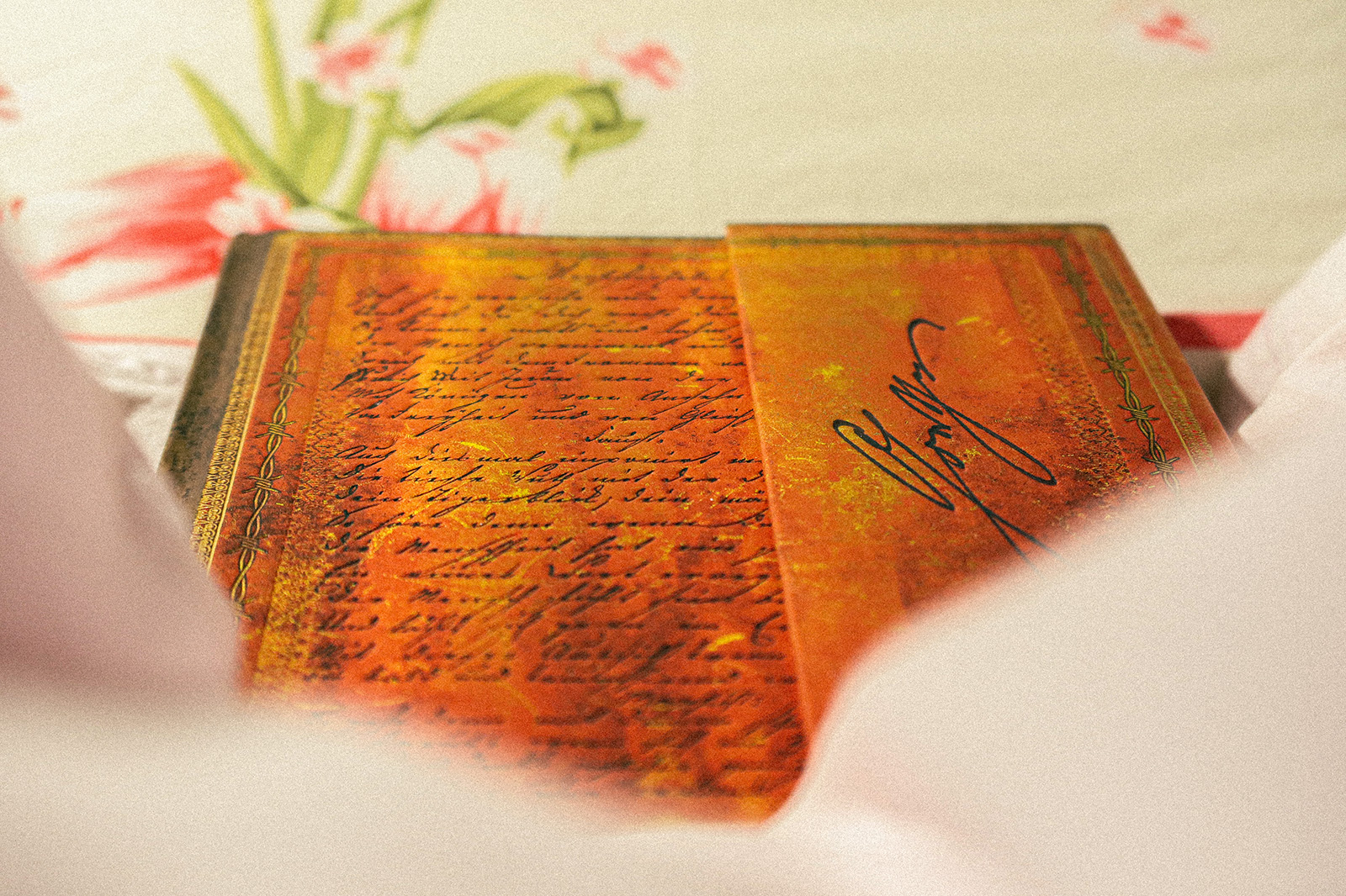 Richly ornamented sketchbook resting on a bed pillow, covered by a blanket.
