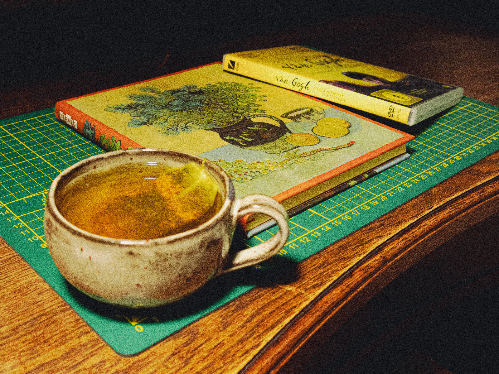 Stoneware teacup, sketchbook with a Van Gogh painting for its cover, and "At Eternity’s Gate" DVD on a wooden desktop.